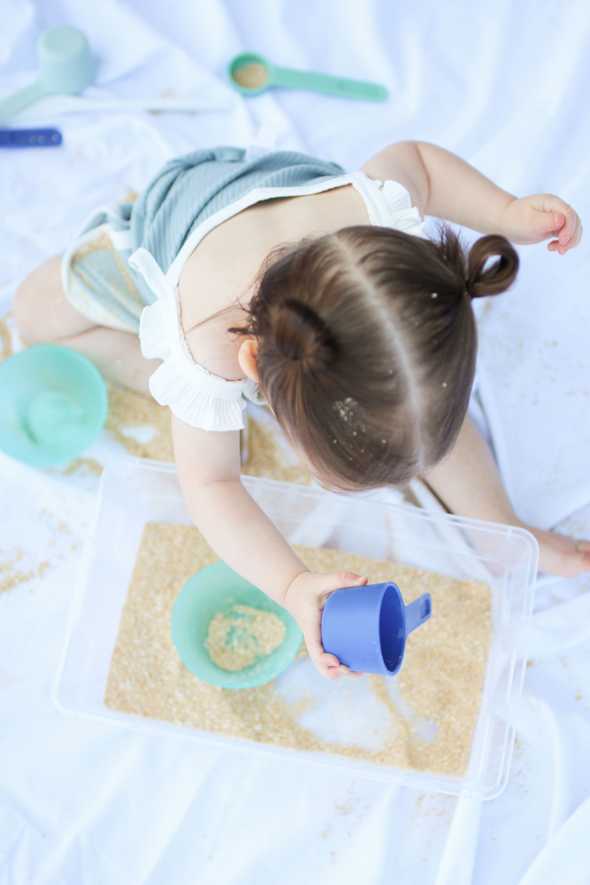 overhead shot of toddler playing with edible sand in a plastic tub