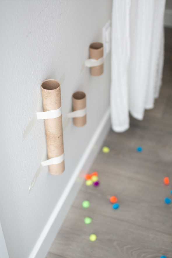 cardboard tubes taped to the wall with pom poms on the floor below