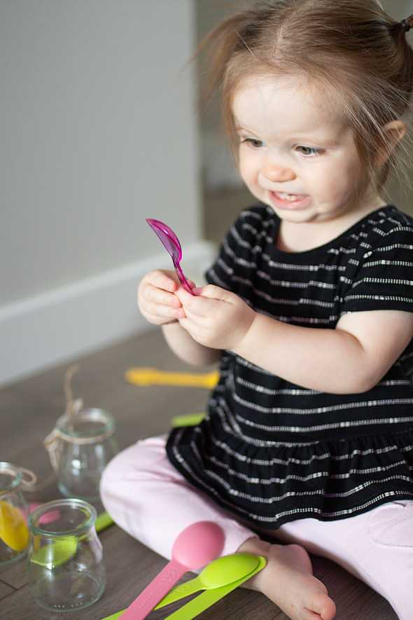 child putting colorful spoons in a jar