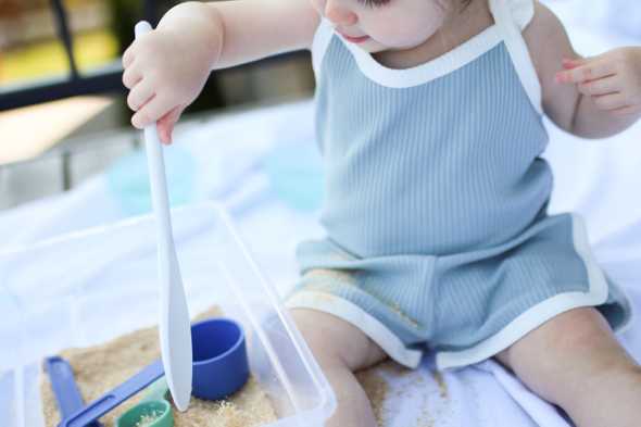 toddler playing with edible sand in a plastic tub