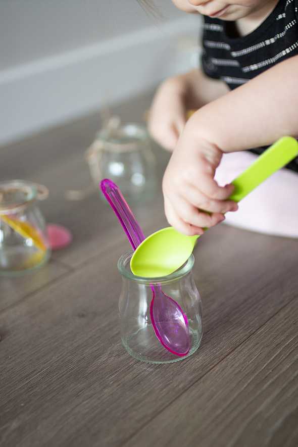 close up of child putting colorful spoons in a jar