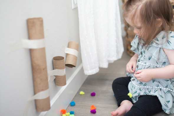 child sitting by pom poms and cardboard tubes taped to the wall