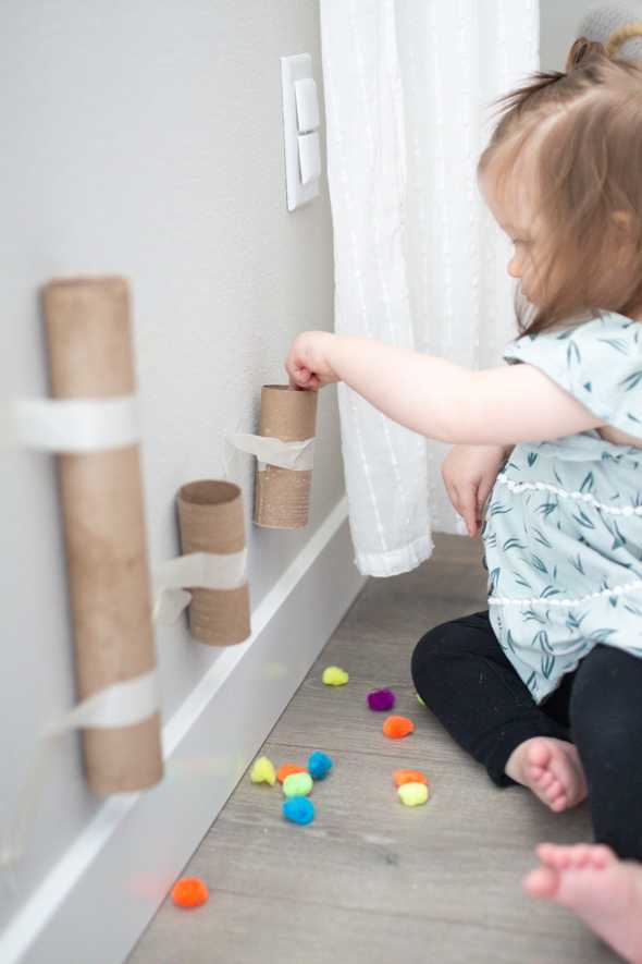 child dropping pom poms in cardboard tubes taped to the wall
