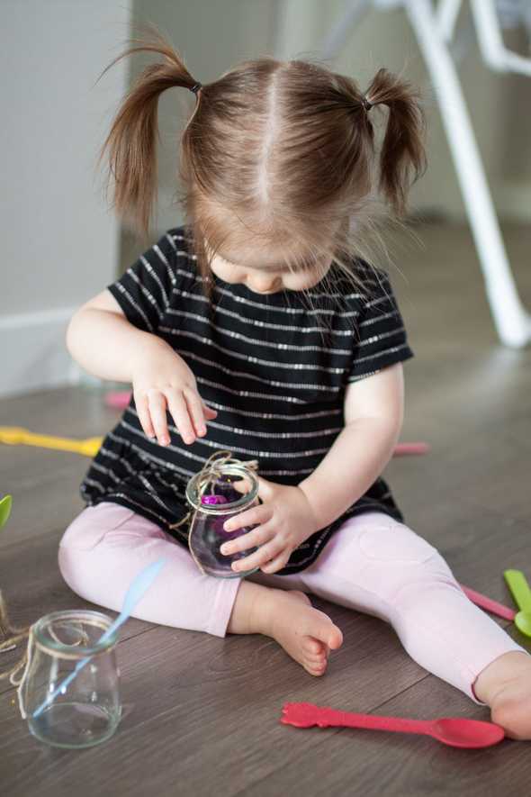 child putting colorful spoons in a jar