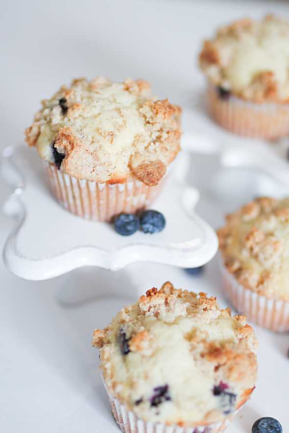 several blueberry streusel muffins surrounded by fresh bluberries